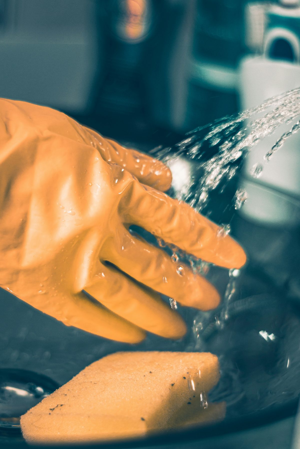 Gloved hand rinsing a sponge under running water - Good Taste Cleaning Services